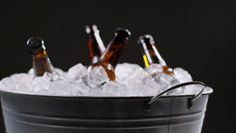 Cerca-De-Botellas-De-Vidrio-De-Cerveza-Fría-O-Refrescos-Enfriándose-En-Un-Cubo-Lleno-De-Hielo-Contra-Fondo-Negro